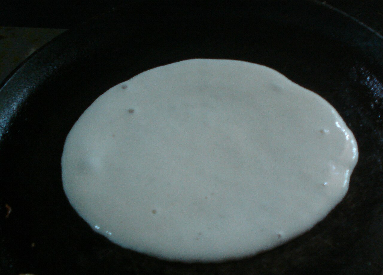 Dosa batter cooking on a hot griddle.